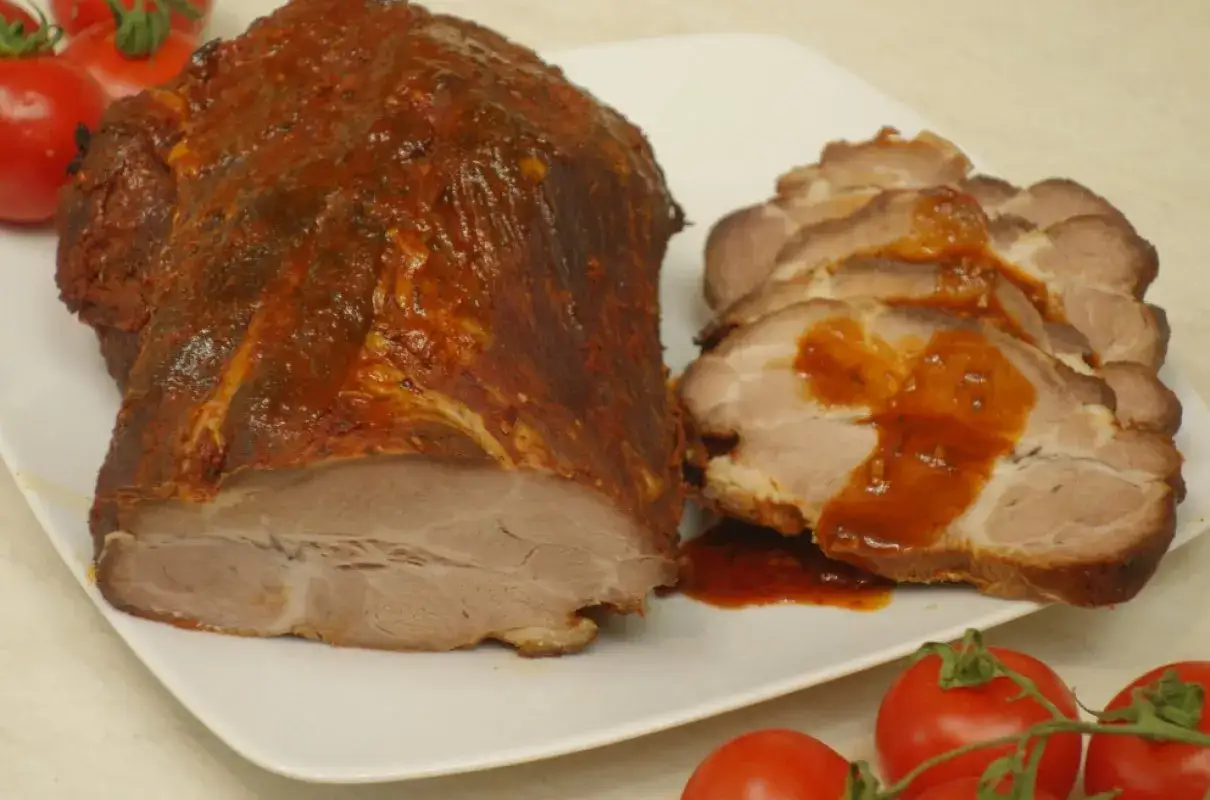 Pieczona karkówka w aromatycznej marynacie, pokrojona w plastry, polana sosem. Obok pomidory.