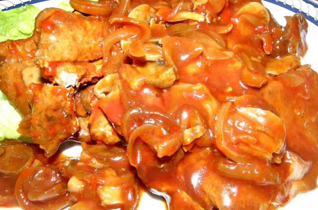 Karkówka z pieczarkami i cebulą w sosie, polana ketchupem, podana na liściach sałaty.