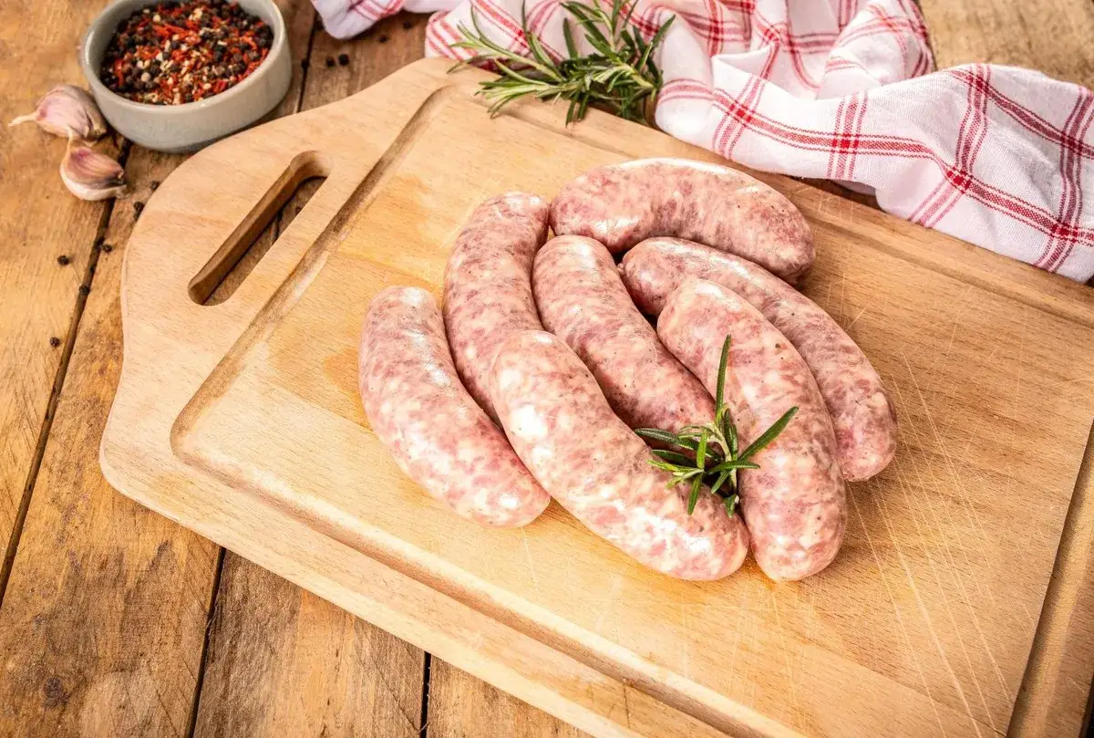 Surowa biała kiełbasa na desce, gotowa do przygotowania. Oto jak ugotować białą kiełbasę, by była pyszna.
