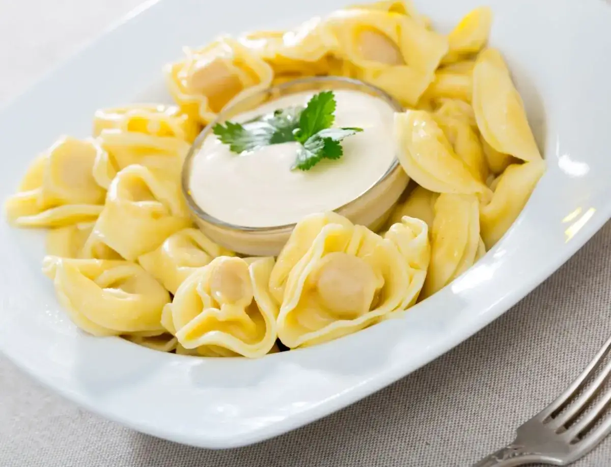 Pyszne tortellini podane z kremowym, aksamitnym sosem śmietanowym do makaronu, udekorowane gałązką natki pietruszki.