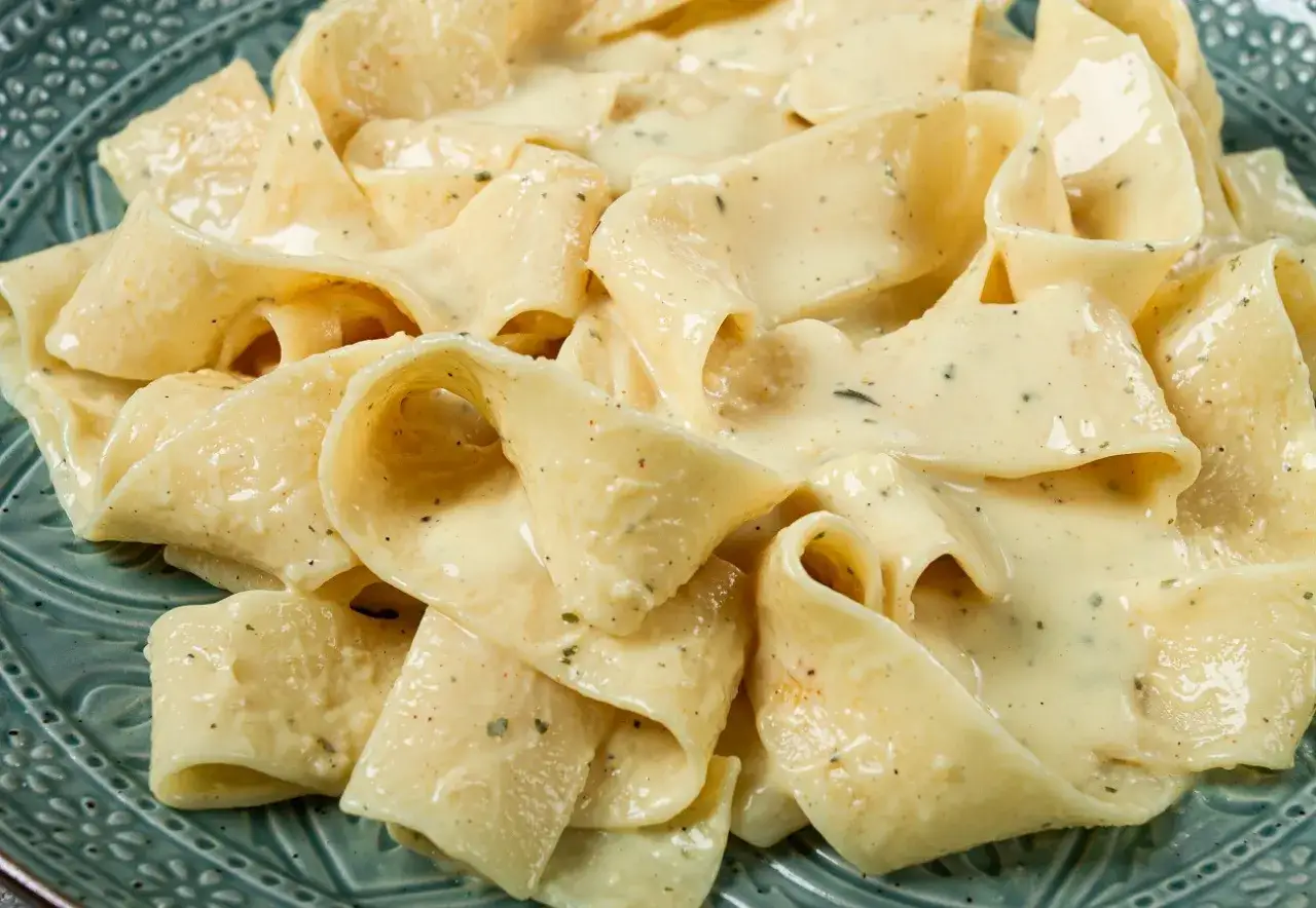 Pappardelle w kremowym sosie śmietanowym, doprawionym ziołami i pieprzem, podane na ozdobnym talerzu.
