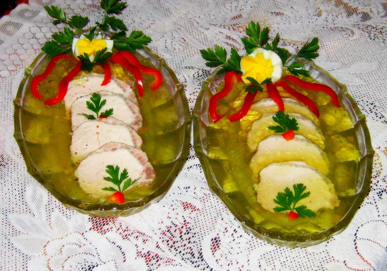 Dwa talerze ze schabem w galarecie, ozdobione jajkiem, papryką i natką. Sprawdzony przepis na schab w galarecie.