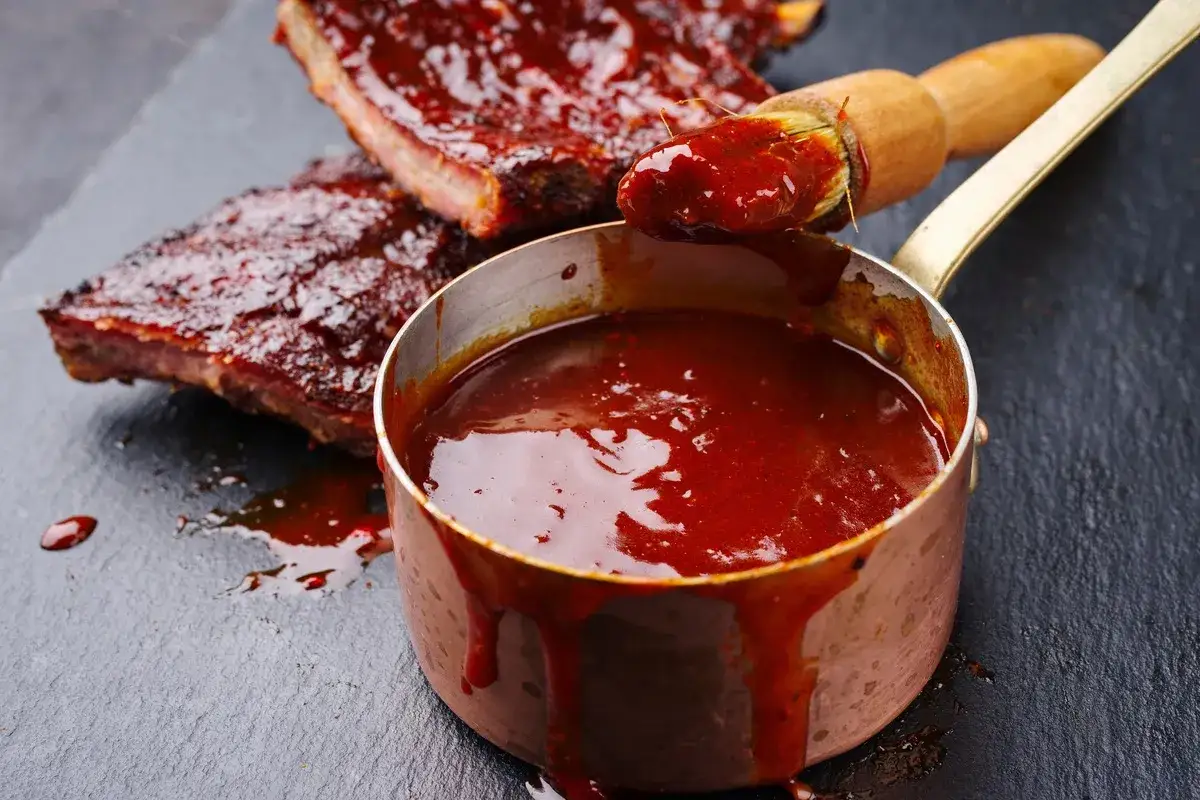 Pyszny, gęsty sos BBQ w miedzianym rondelku, idealny do żeberek. Pędzelek zanurzony w sosie sugeruje, jak zrobic sos do zeberek.