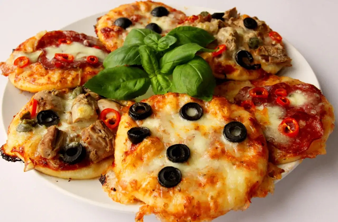 Pizzerinki z gotowego ciasta do pizzy: mini pizze z salami, oliwkami, papryczką chili i bazylią na talerzu.