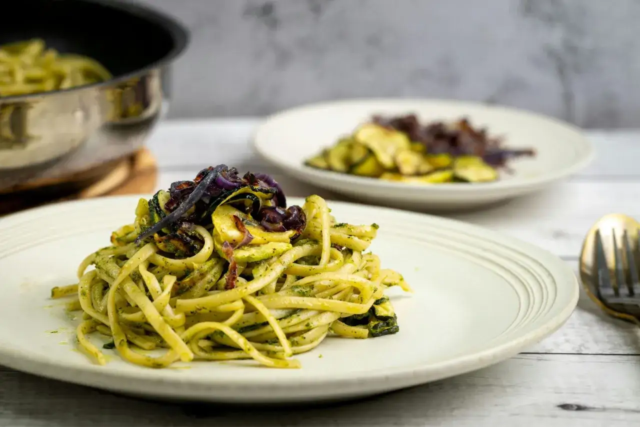Szybkie dania z cukinią: makaron z zielonym pesto, grillowaną cukinią i czerwoną cebulą na talerzu.