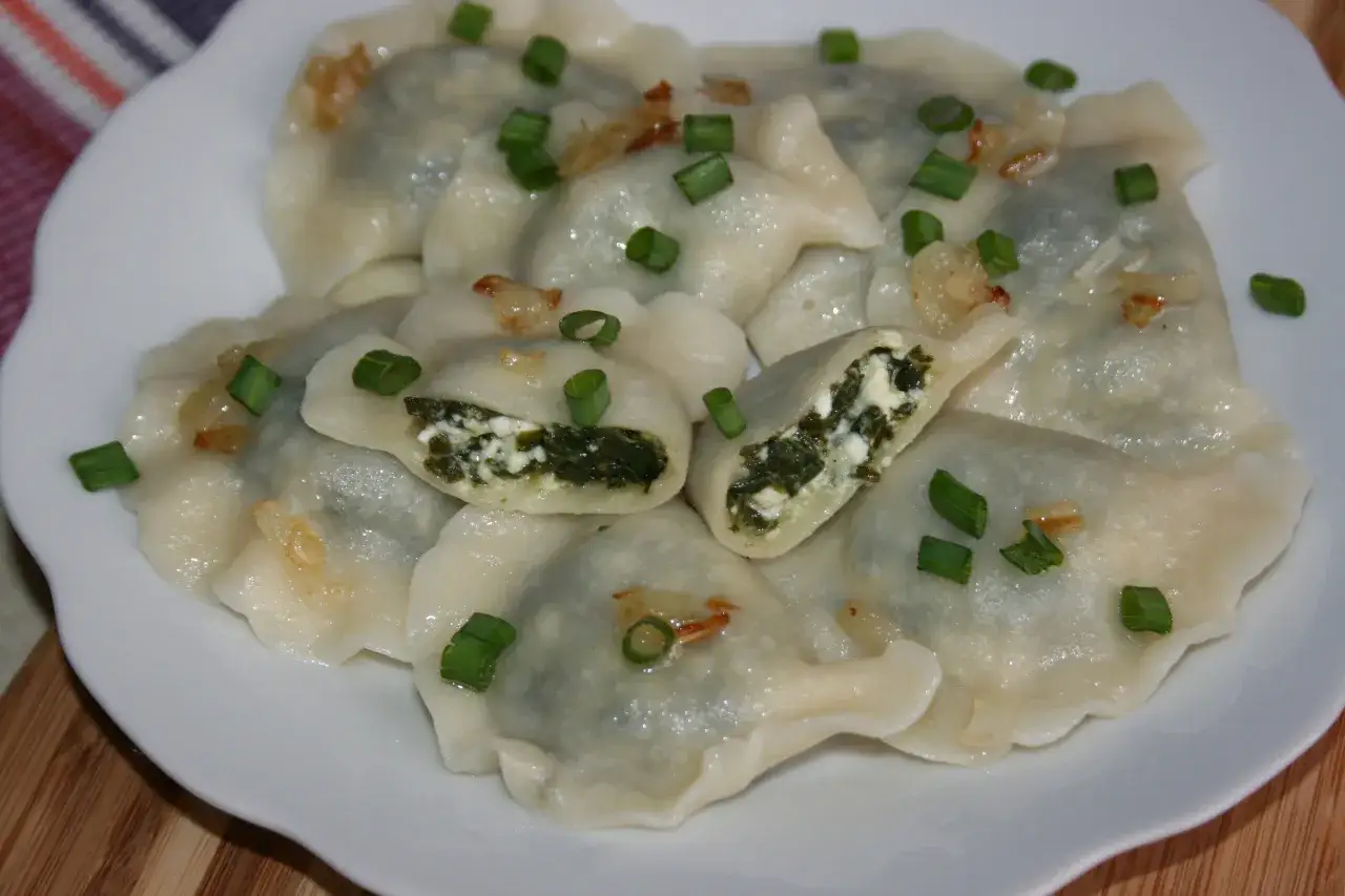 Pyszne pierogi z farszem ze szpinaku i białego sera, posypane szczypiorkiem i skwarkami.