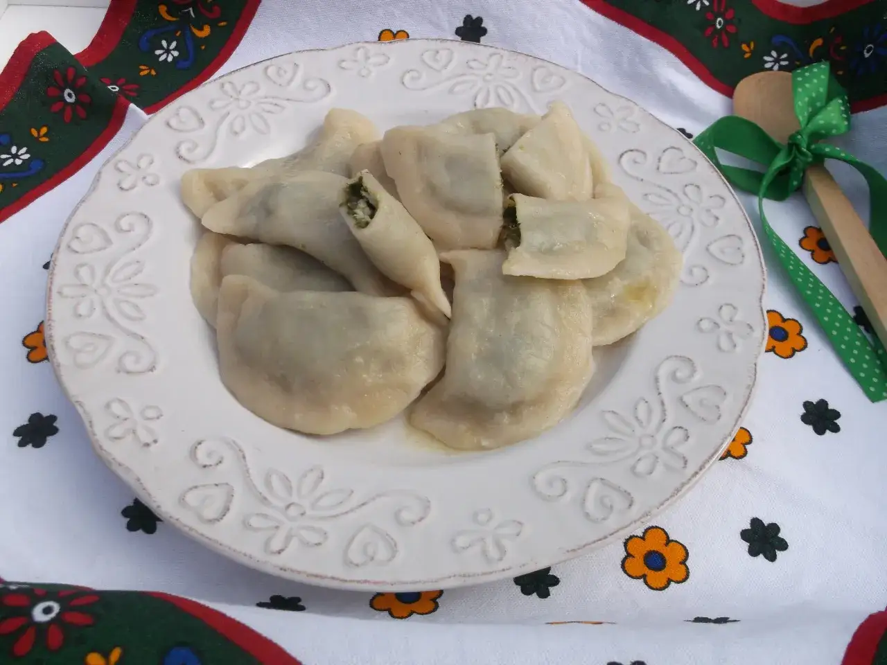 Pyszne pierogi z farszem ze szpinaku, podane na talerzu z tradycyjnym wzorem.