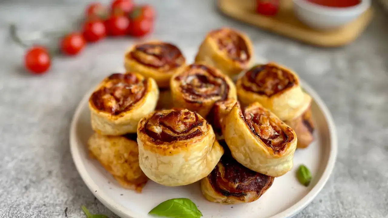 Pizzerinki z gotowego ciasta do pizzy, zwinięte w apetyczne rolki, z pomidorkami i bazylią w tle.