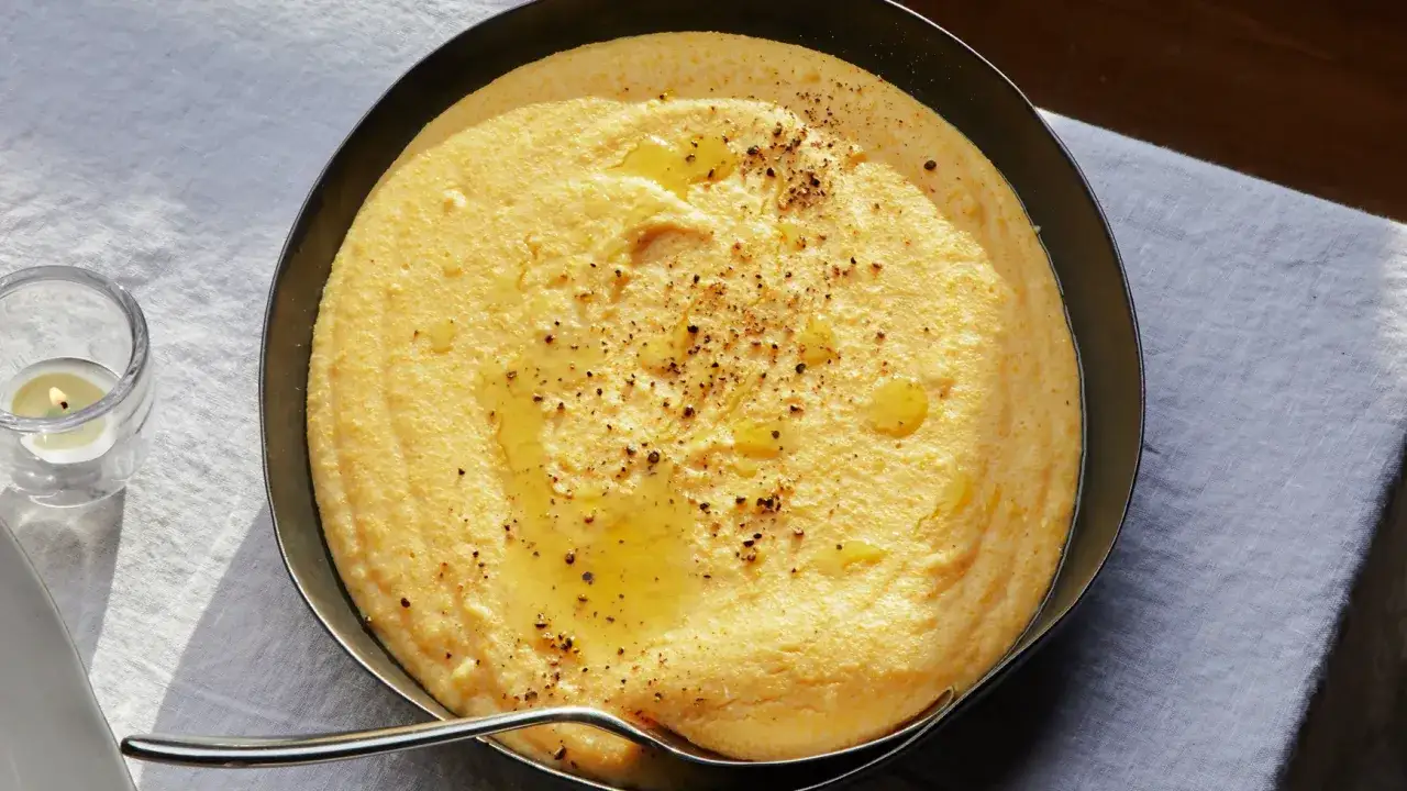 Ciepła polenta z mąki kukurydzianej, polana oliwą i posypana pieprzem, podana w metalowej misce. Obok pali się świeca.