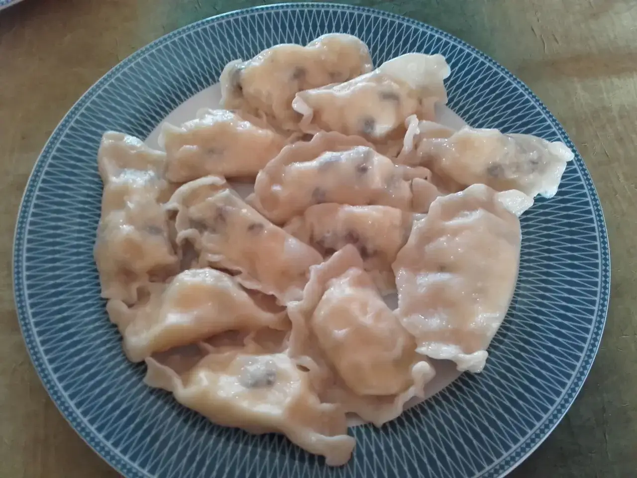 Talerz pełen pierogów z serem, których farsz wygląda na domowy i pyszny.