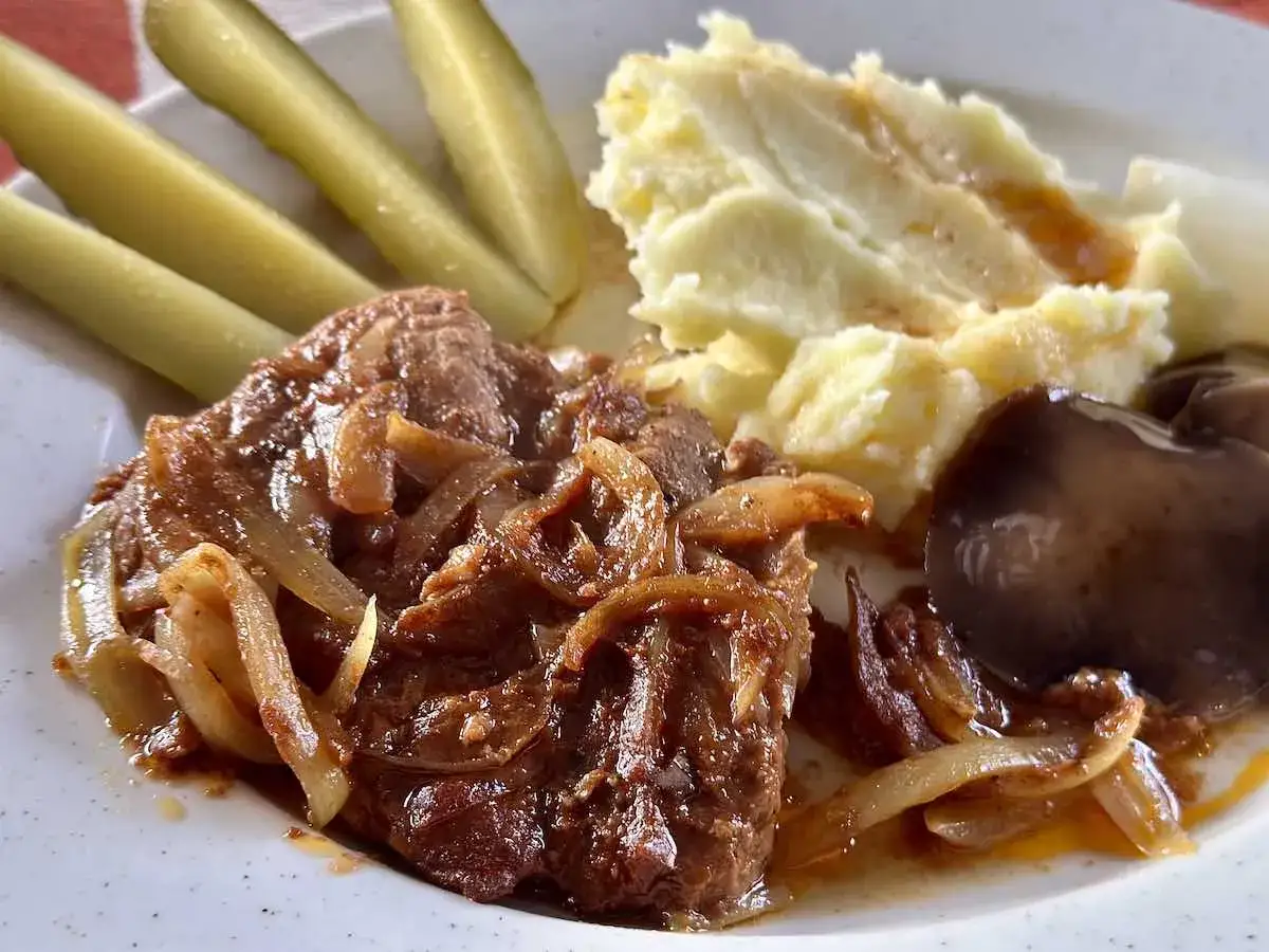 Soczysta karkówka z piekarnika duszona z cebulką, podana z puree ziemniaczanym, ogórkami kiszonymi i pieczarką.