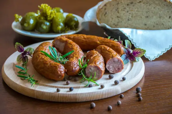 Swojska kiełbasa na desce z rozmarynem i pieprzem. Obok ogórki i chleb. Idealna ilość soli do kiełbasy swojskiej.