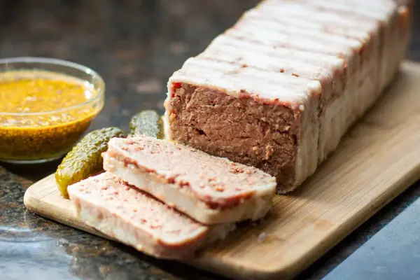 Pasztet zawinięty w boczek, pokrojony na plastry, z ogórkami i musztardą. Idealny do pieczenia w temperaturze 160°C.
